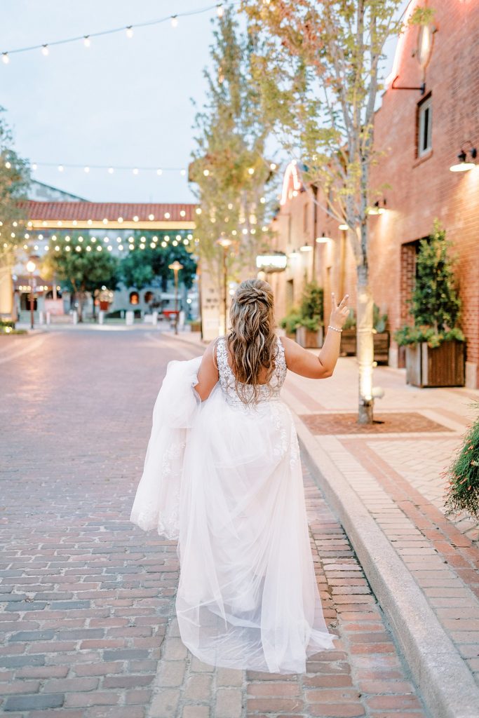 Bride standing on brick path holding up peace sign