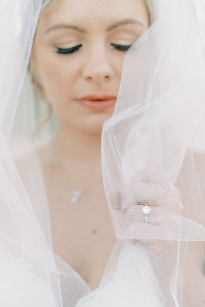 Bride holding up engagement ring under wedding veil