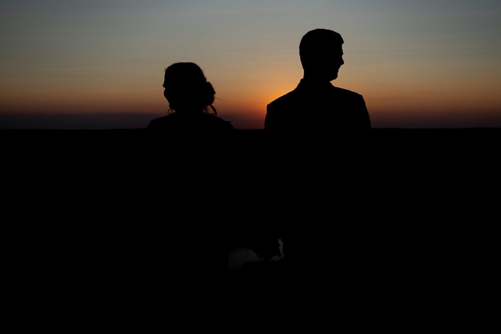 BW bride and groom holding hands looking opposite directions at sunset
