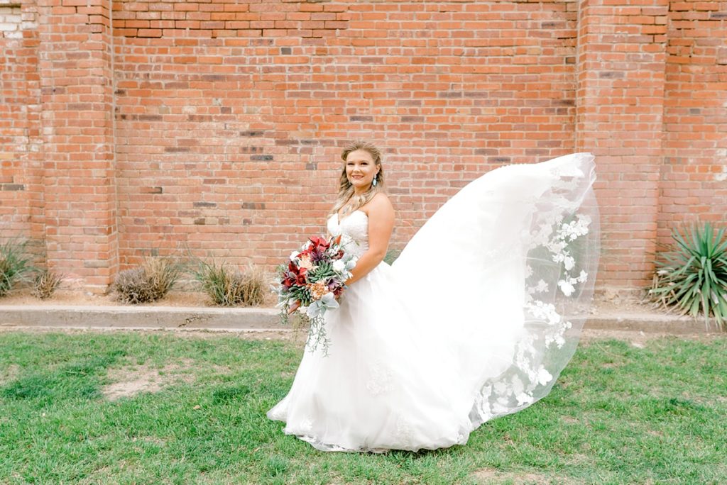 Bride standing in front of brick wall with sweeping veil I Fort Worth Stockyards bridal session