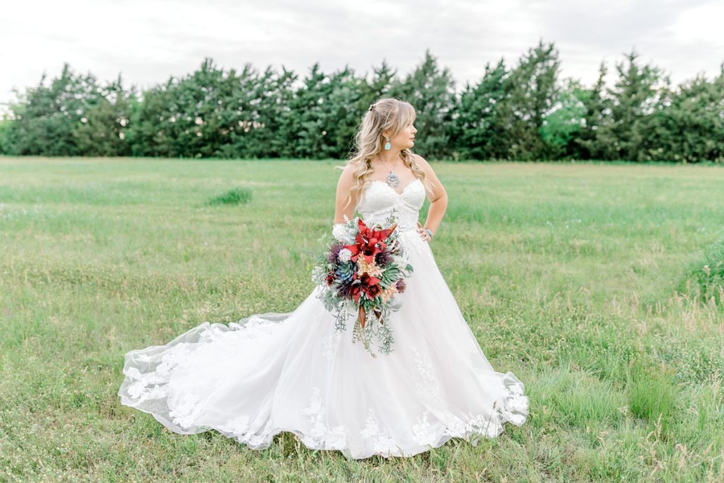 Bride standing in field with red wildflower bouquet