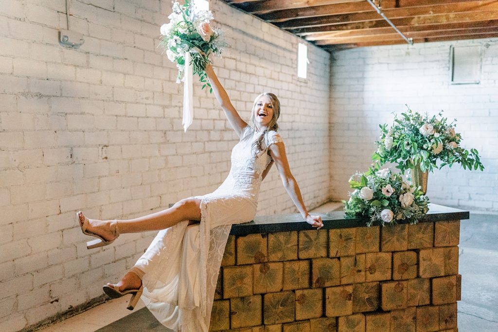 Bride sitting on countertop holding up bouquet