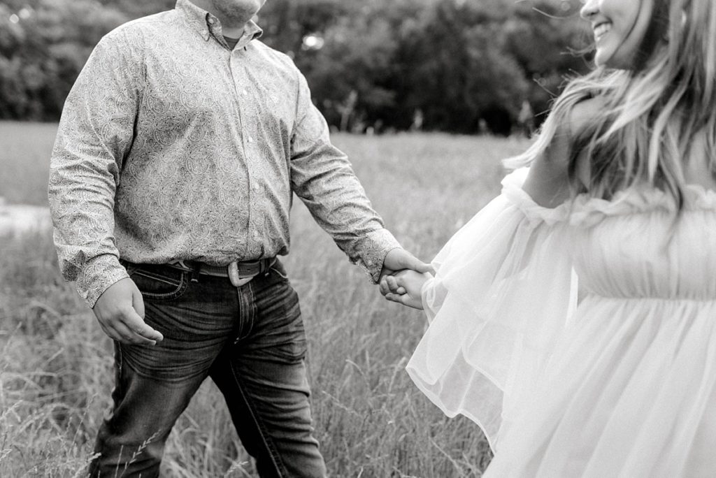 couple holding hands walking through field