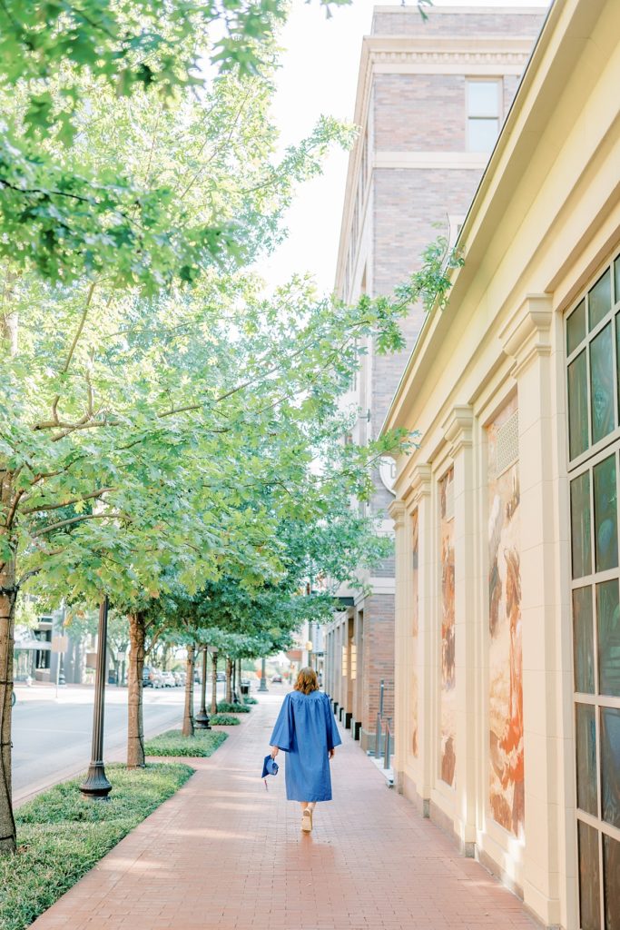 girl walking down brick sidewalk in cap and gown in 2021 high school senior session