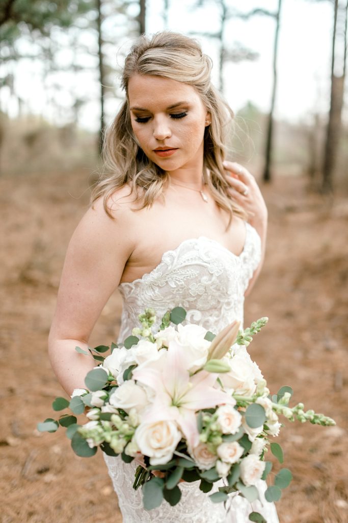 Bride looking down holding floral bouquet in woodsy bridal session Texas