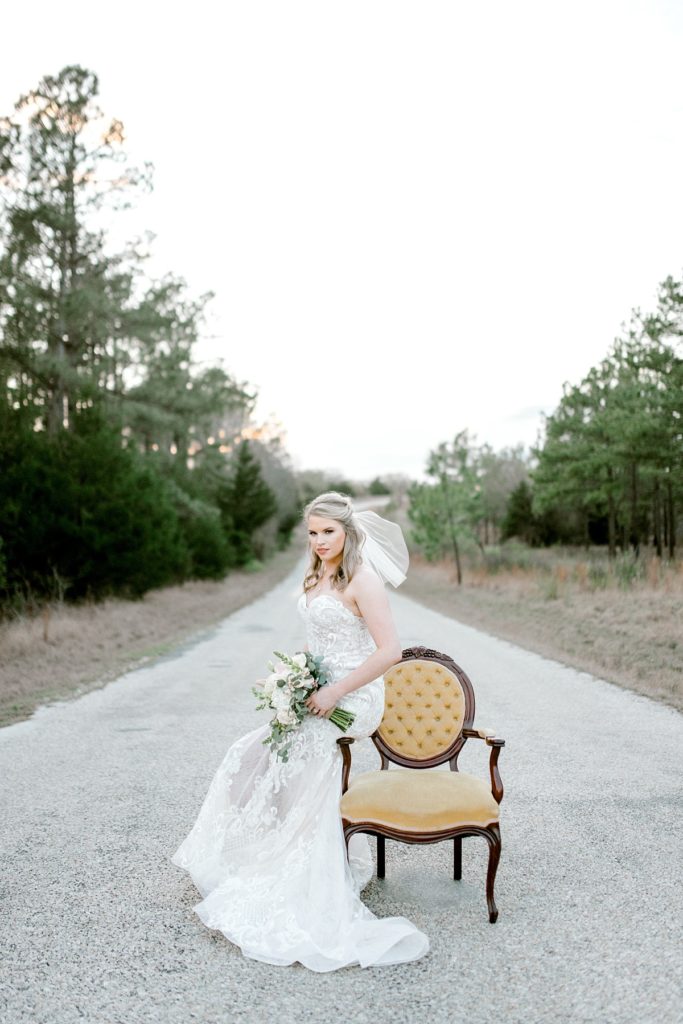 bride leaning against vintage chair in middle of road for woodsy bridal session Texas