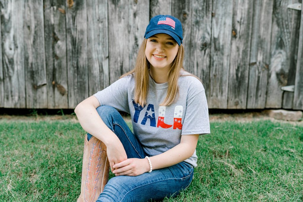 Girl sitting in grass wearing American flag cap for Timber Creek senior session