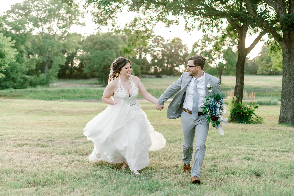 Bride and groom holding hands running through field at The Hamptons at Weatherford Texas wedding