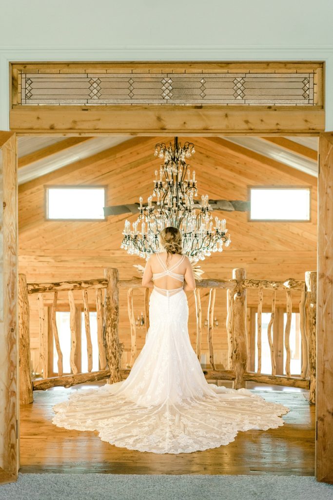 Bride standing on balcony of Diamond H3 Ranch reception hall with large chandelier Texas bridal session