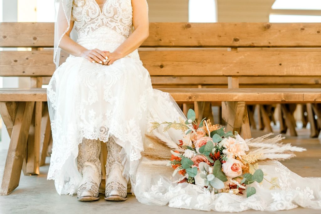 Bride sitting on bench revealing Bridal boots and rustic chic bridal bouquet Diamond H3 Ranch Texas bridal session