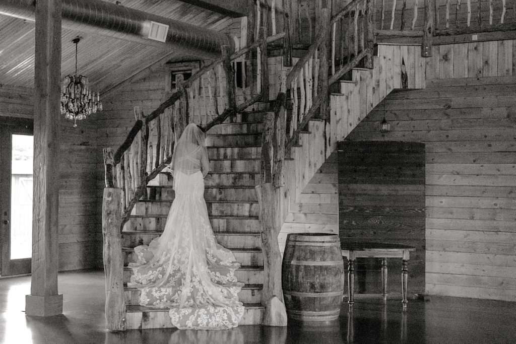 BW bride standing on stairs with wedding gown train flowing down behind her Diamond H3 Ranch Texas bridal session