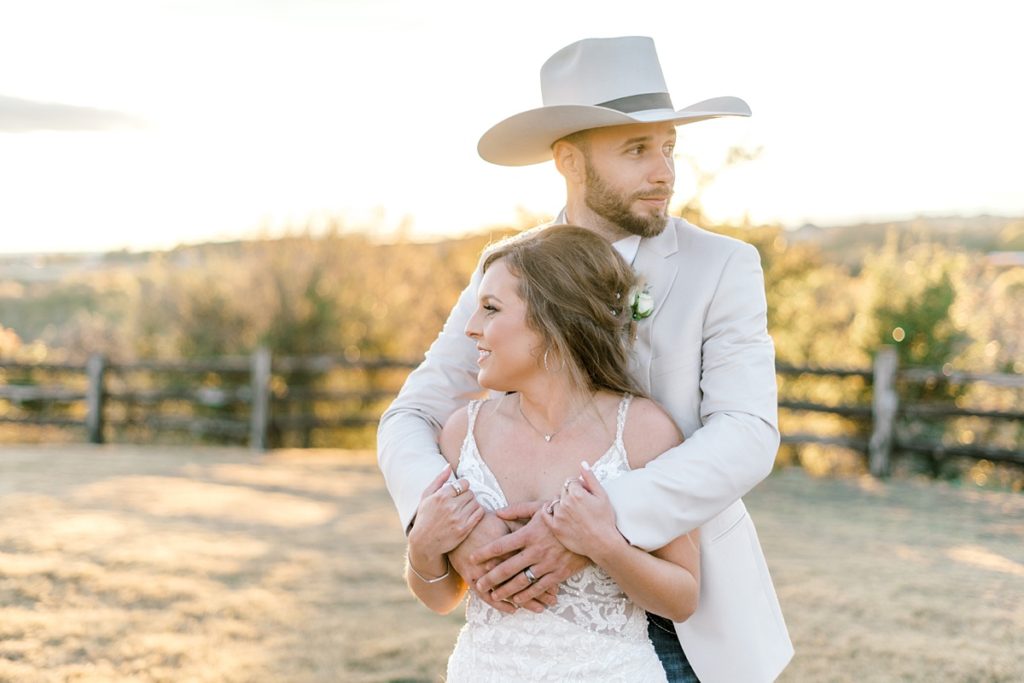 groom hugging bride from behind in golden hour sunlight Diamond H3 Ranch wedding